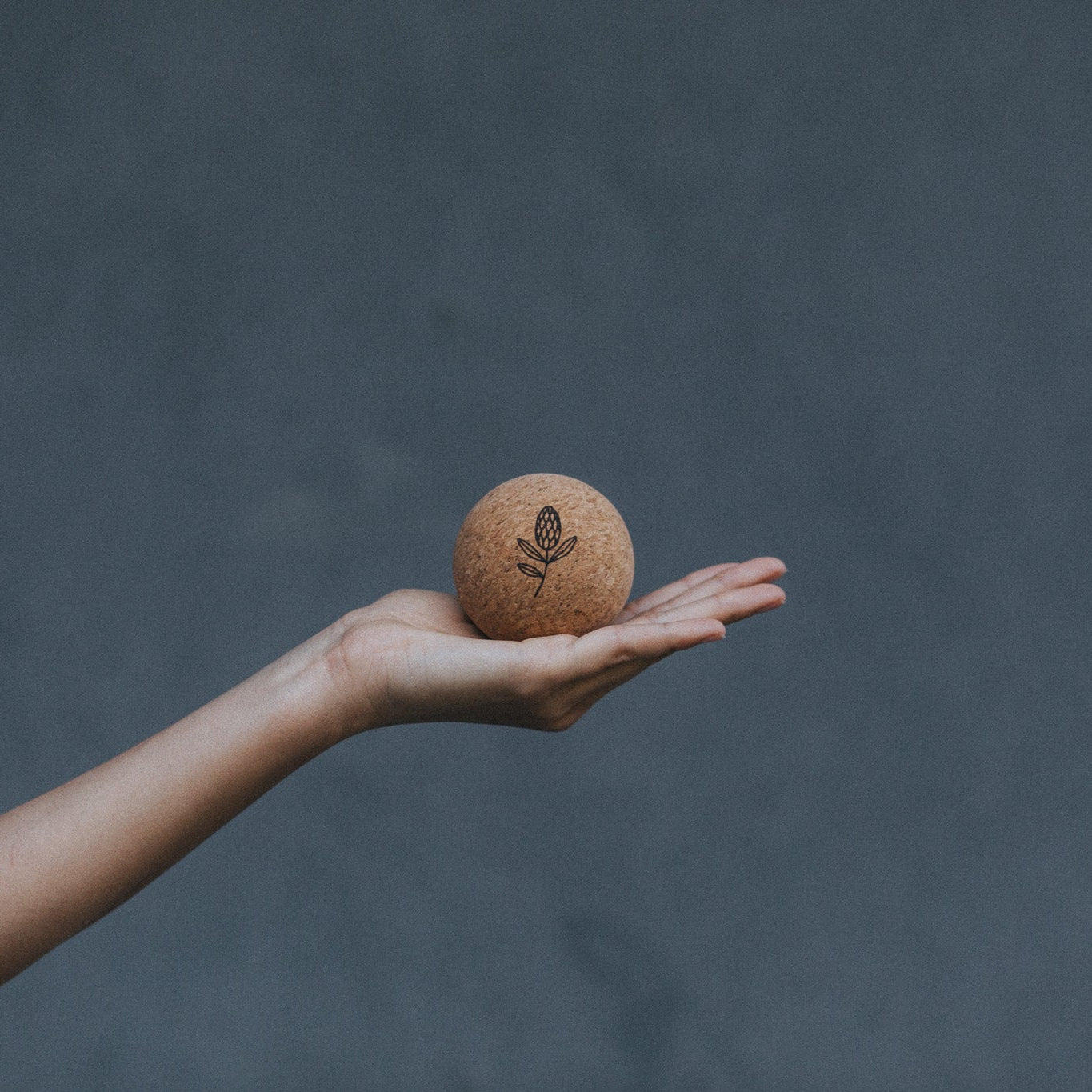 Hand holding a cork yoga ball against a dark grey background