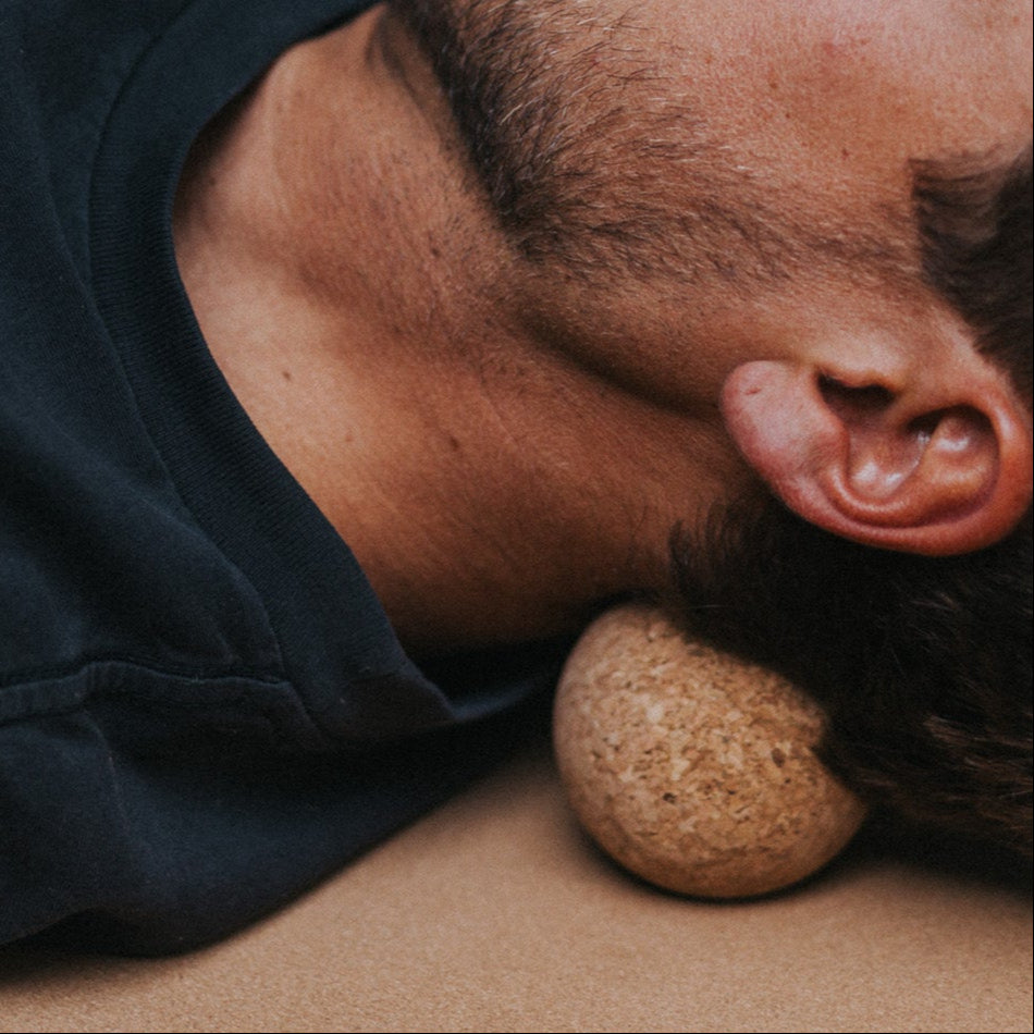 Man lying down with a cork massage roller on his neck laying on a cork mat.