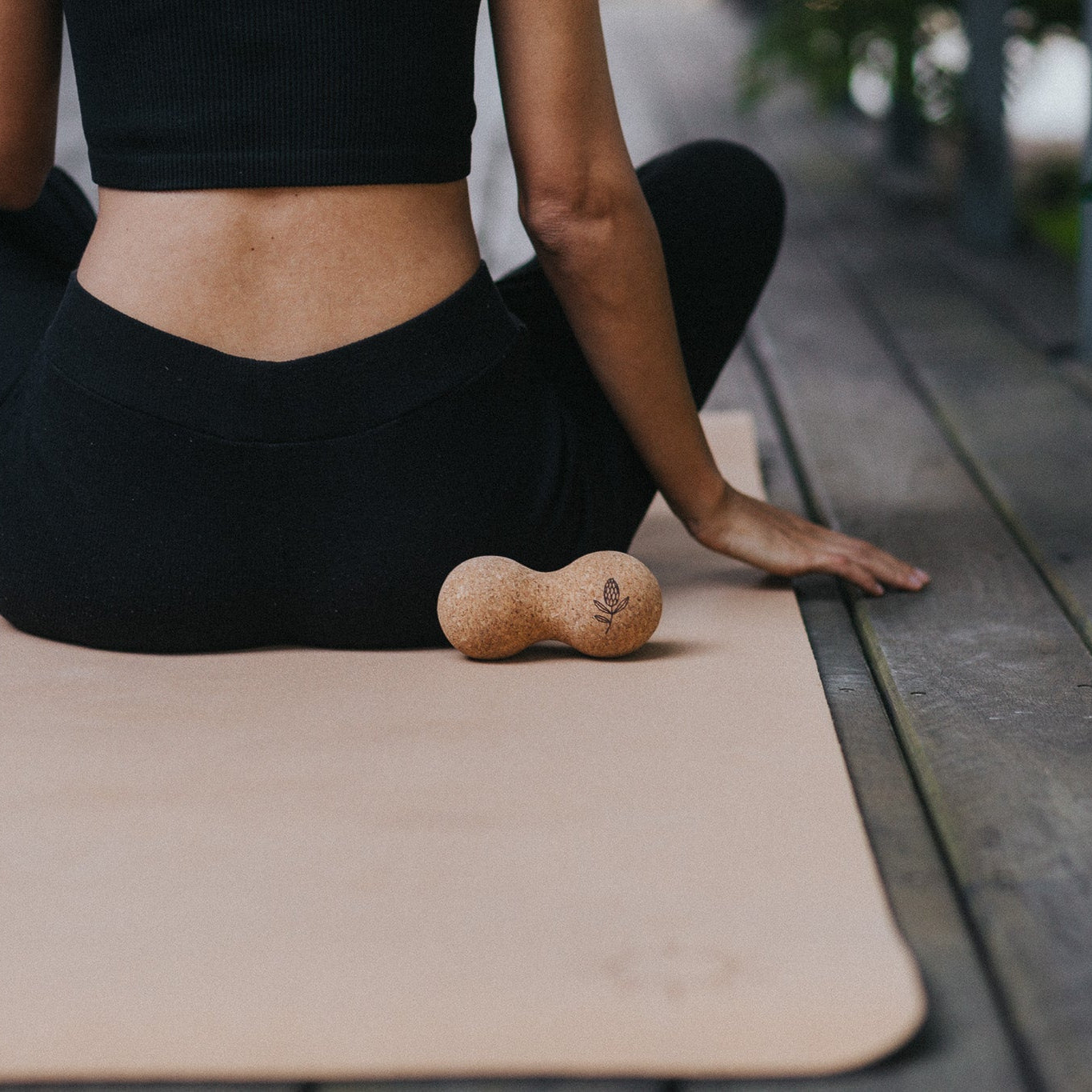 Person sitting on a yoga mat with a cork yoga ball, outdoors.