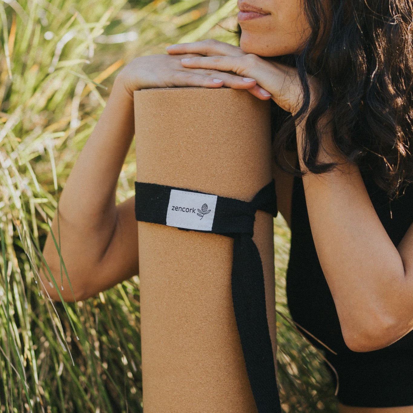 Person holding a cork yoga mat with a strap outdoors
