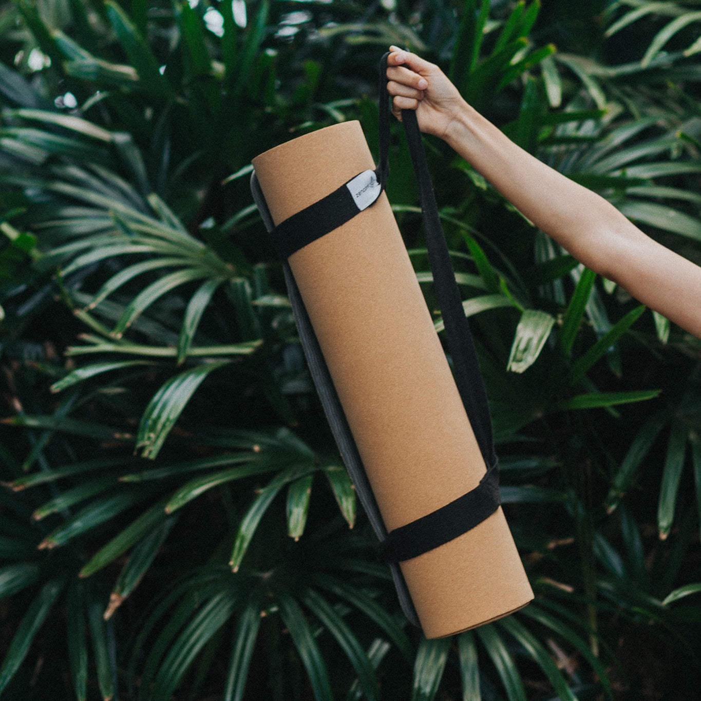 Yoga mat with straps held by a hand against a green leafy background
