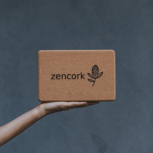Hand holding a brown cork block with 'zencork' branding against a dark background