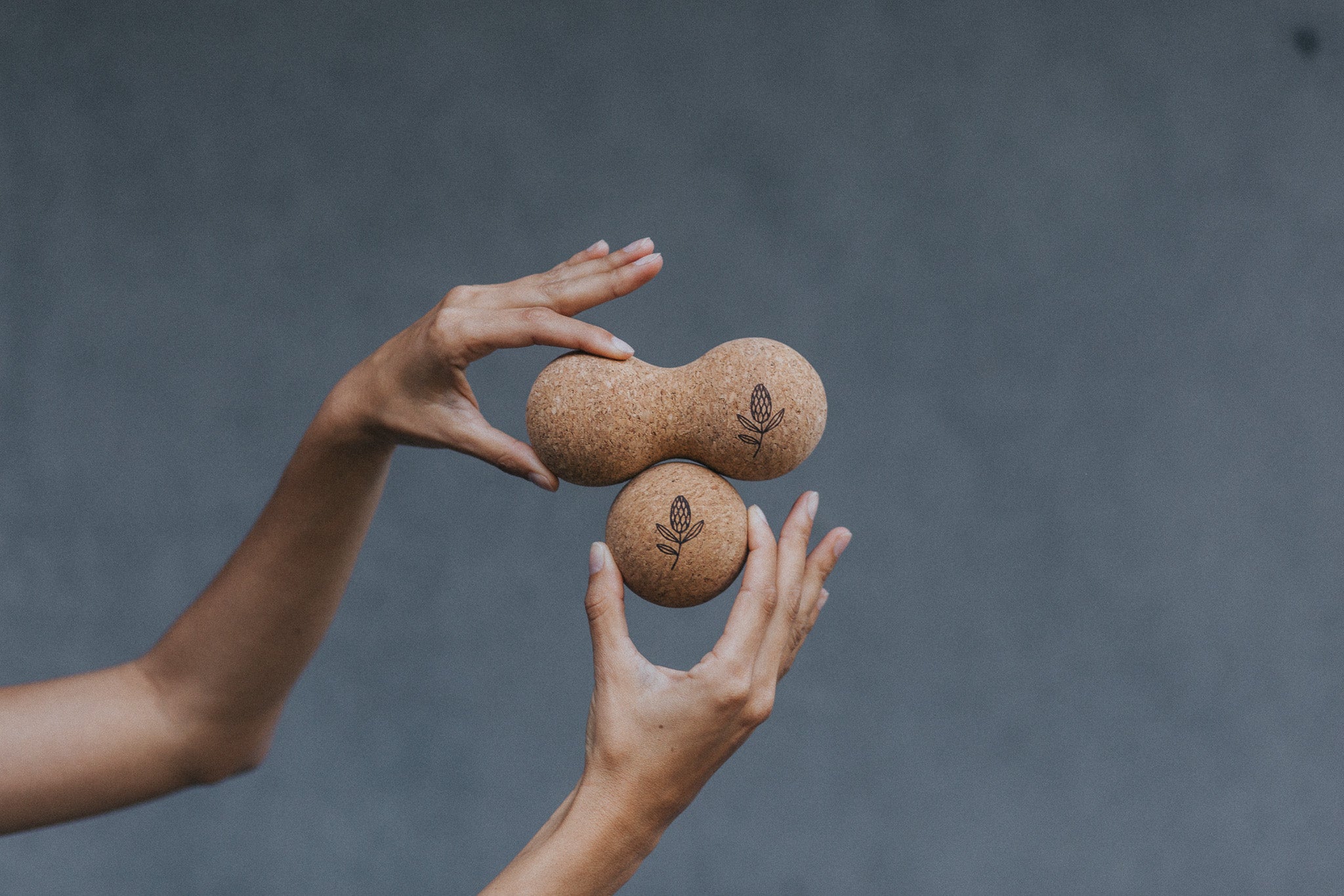 Two hands holding two brown stones with a subtle pattern against a dark gray background