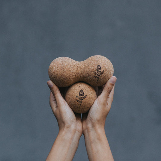 Two hands holding two brown cork massage balls
