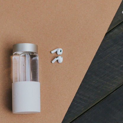 clear glass water bottle with earphones on a yoga mat on a wooden floor