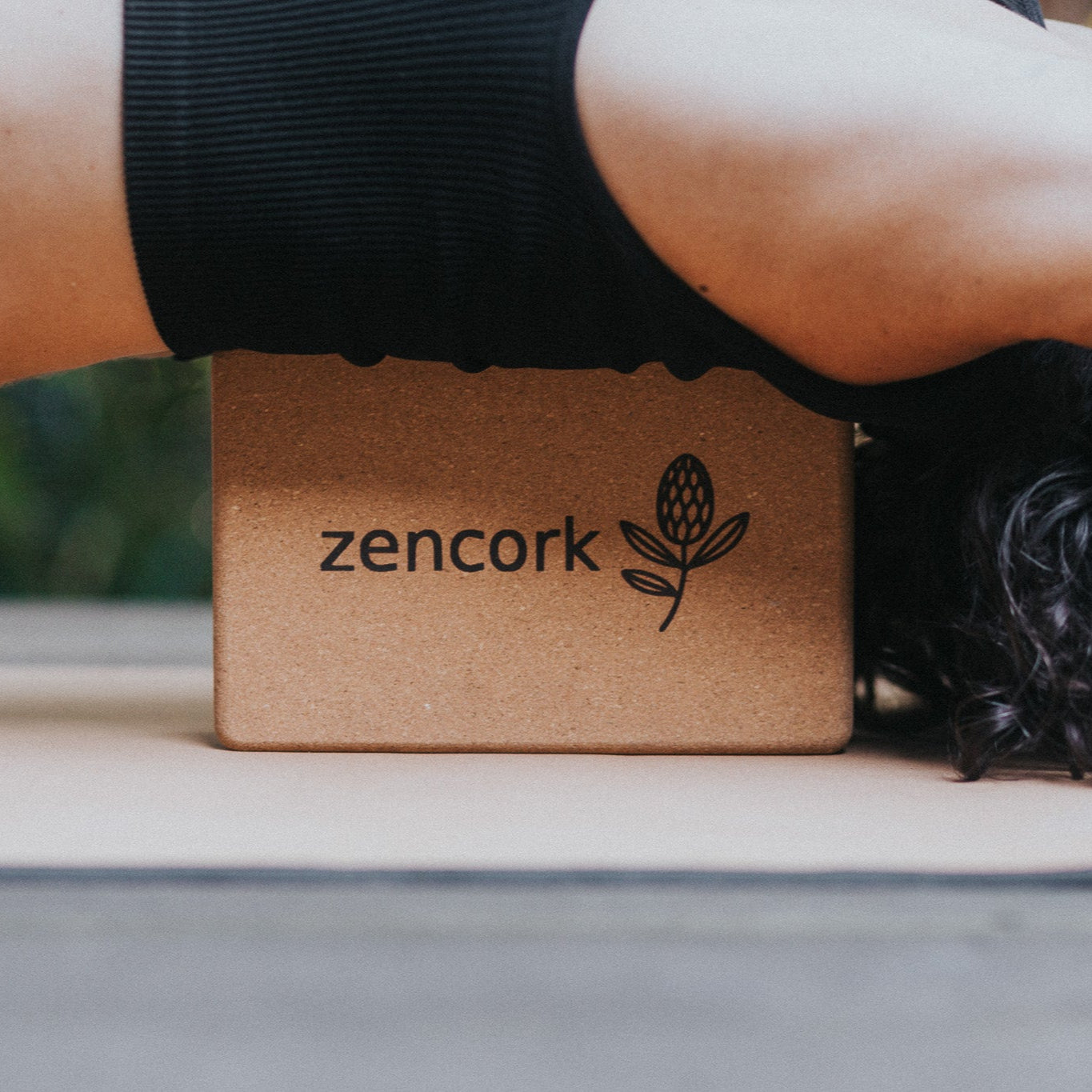 Person lying on a yoga mat with a Zencork yoga block under their head.