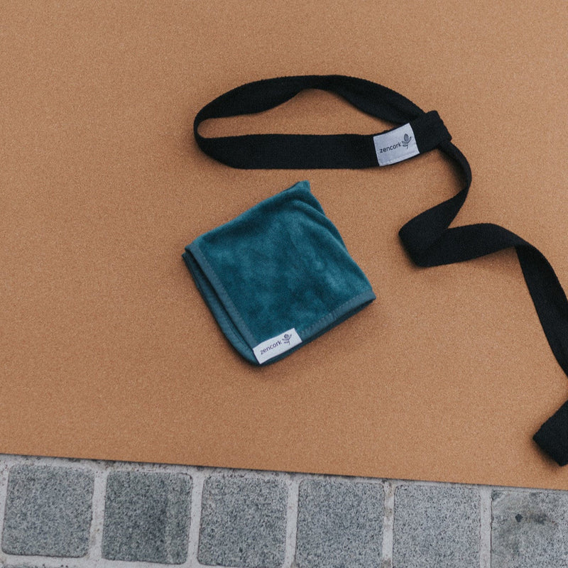Teal towel and black strap on a brown mat with a tiled floor background
