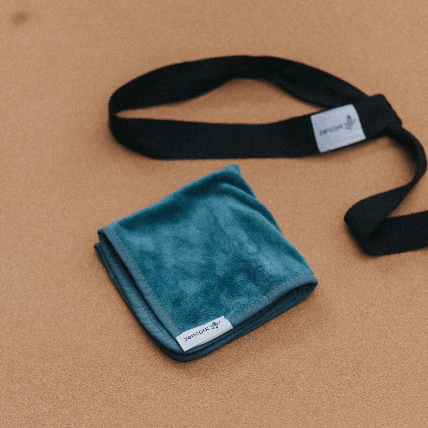 Tourqoise microfibre cloth with black branded straps on a cork yoga mat.