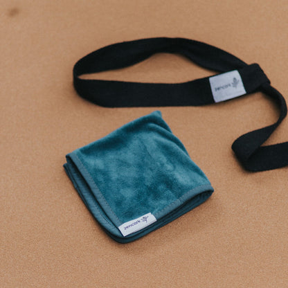 Tourqoise microfibre cloth with black branded straps on a cork yoga mat.