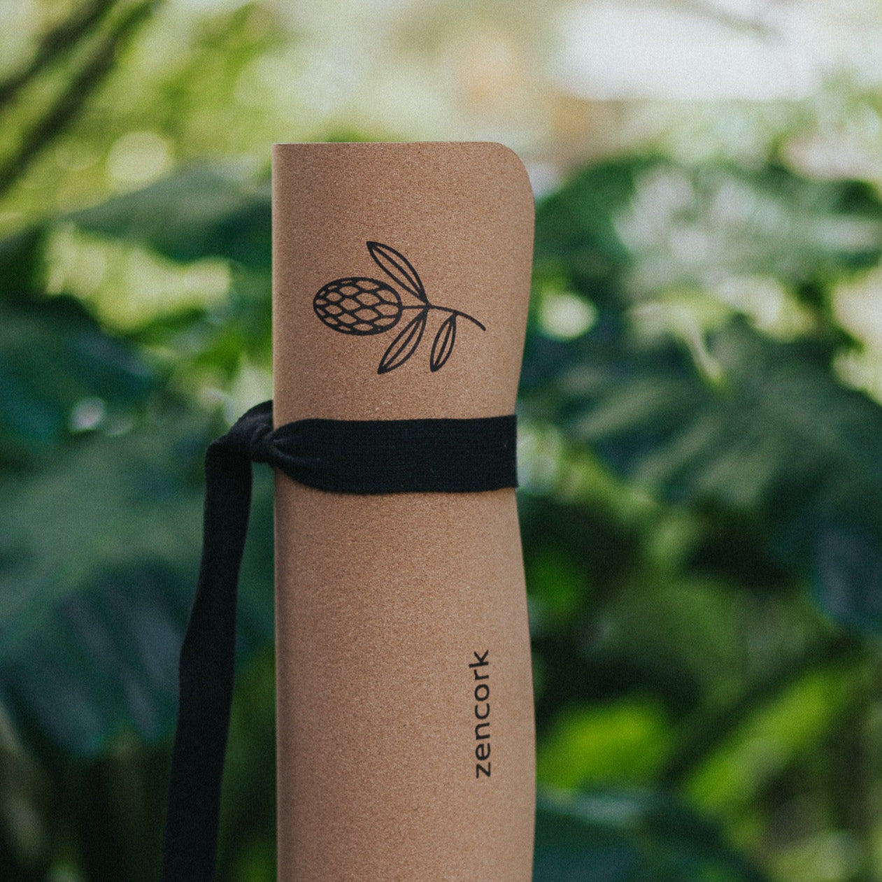 Cork yoga mat with black strap on a wooden surface with green foliage in the background
