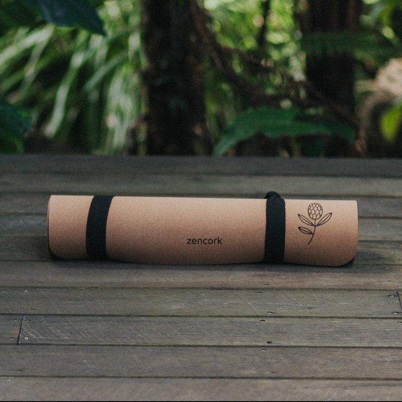 Roll-up cork yoga mat with black straps on a wooden surface in a natural setting