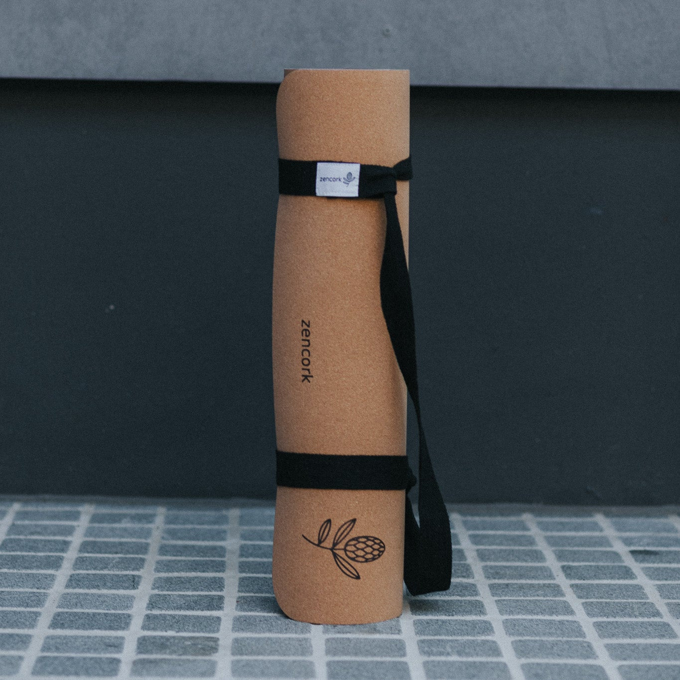 Cork yoga mat with a black strap on a gray tiled floor
