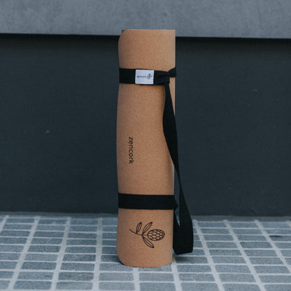 Cork yoga mat with a black strap on a gray tiled floor