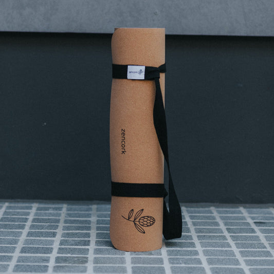 Cork yoga mat with a black strap on a gray tiled floor