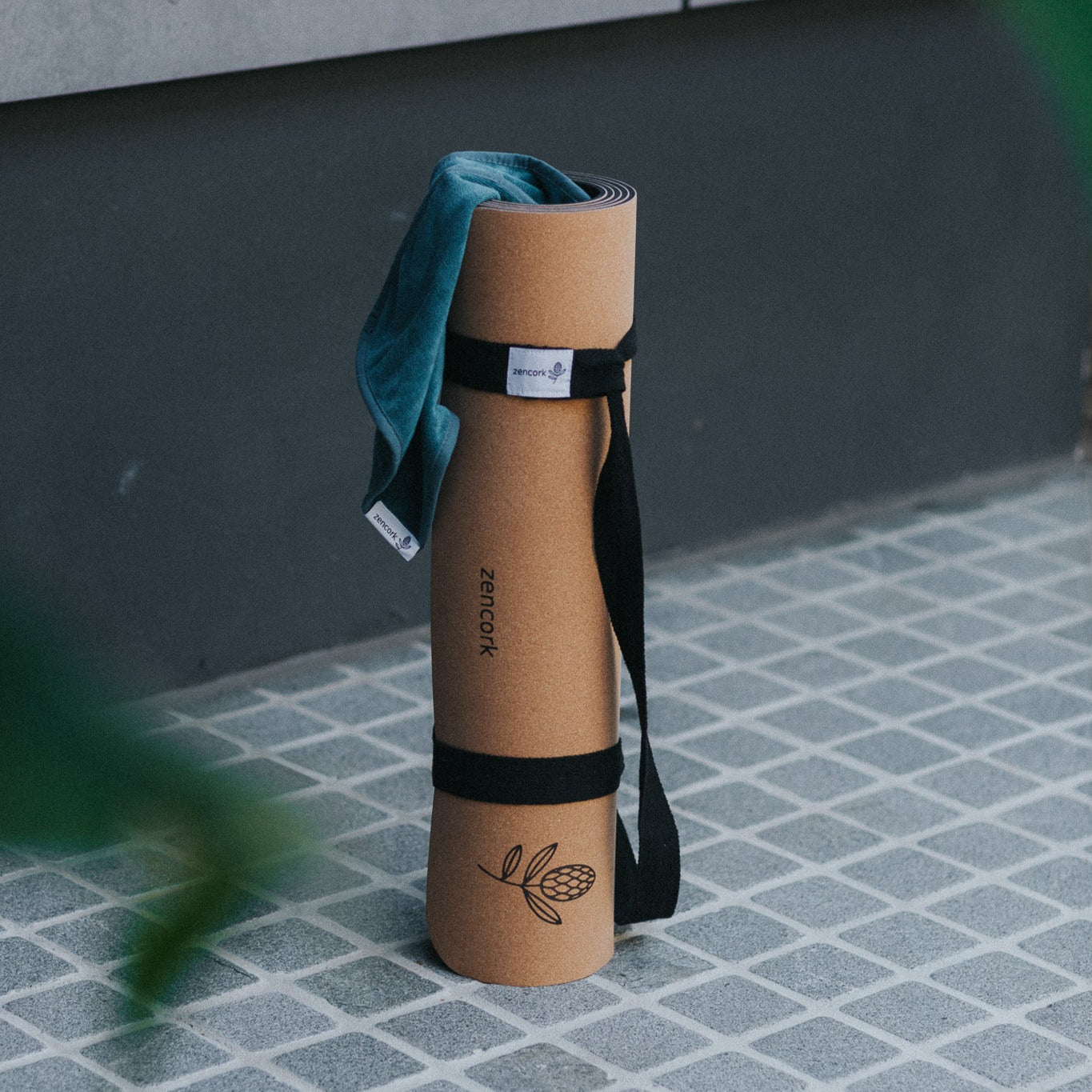 Brown yoga mat with a black strap and blue towel on a tiled floor